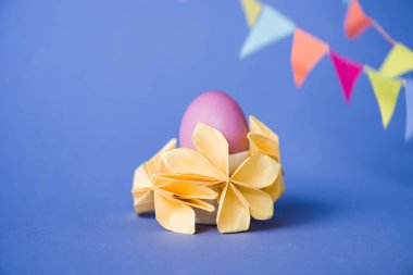 Origami çiçeklerinin seçici odak noktası mavi üzerine paskalya yumurtası. 