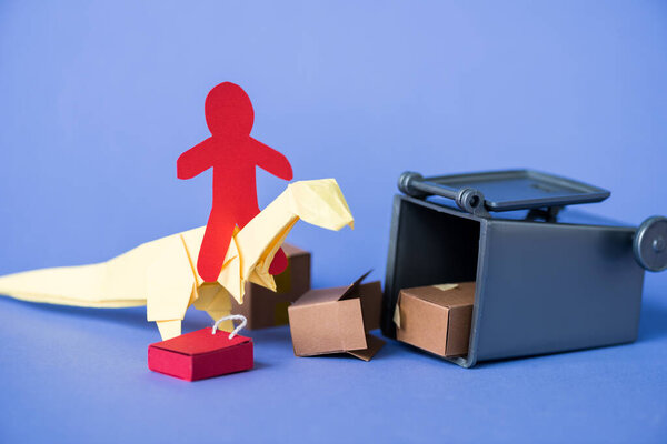 paper human on origami dinosaur near trash can and carton boxes on blue 