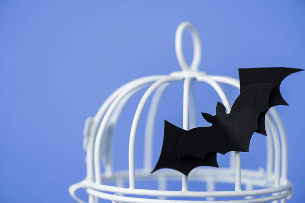 selective focus of origami bat near metallic cage isolated on blue 
