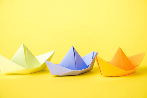 colorful paper ships on yellow with copy space 