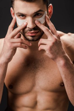 Seksi çıplak adam gri üzerine izole edilmiş yüzüne göz bandı yapıştırıyor.