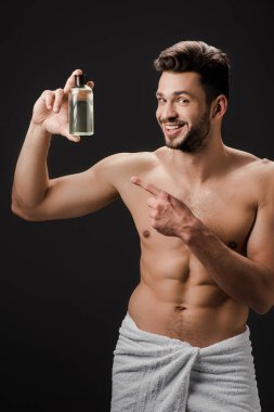 Siyah üzerine izole edilmiş bir parfüm şişesini gösteren seksi, neşeli adam.