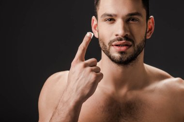 Yakışıklı çıplak adam siyah üzerine izole yüz kremi sürüyor.