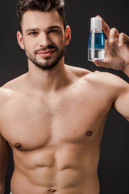 Seksi sakallı çıplak adam elinde kozmetik sıvıyla siyah şişeyi tutuyor.