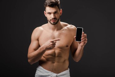 Havlu giymiş seksi adam gri ekranlı akıllı telefonu işaret ediyor. 