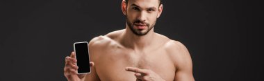 Siyah ekranda beyaz ekranlı akıllı telefonu işaret eden seksi çıplak adamın panoramik görüntüsü 