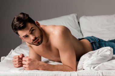 Kotlu seksi, üstsüz, sakallı adam gri yatakta yatıyor.