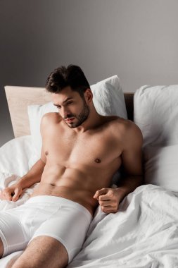 Sakallı yakışıklı seksi adam gri yatakta yatıyor.