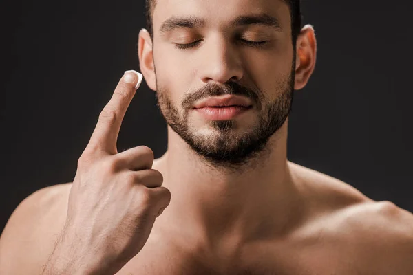 Homem Barbudo Com Olhos Fechados Aplicando Creme Facial Isolado Preto — Fotografia de Stock