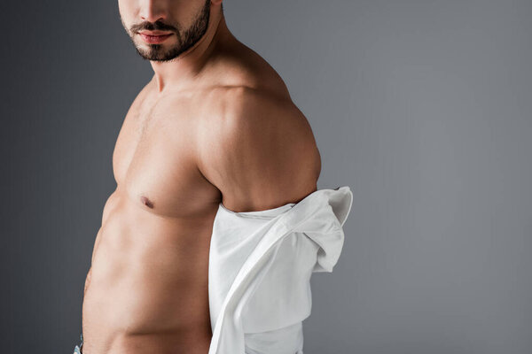 обрезанный вид сексуального мускулистого мужчины в белой рубашке на сером
