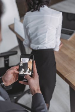 Akıllı telefondan sekreterin kalçalarının fotoğrafını çeken işadamı görüşü.