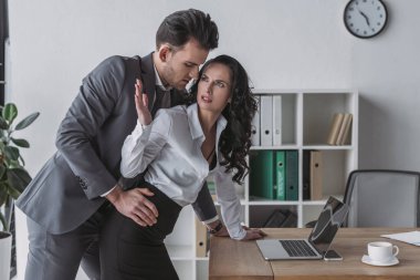 handsome businessman molesting angry secretary in office clipart