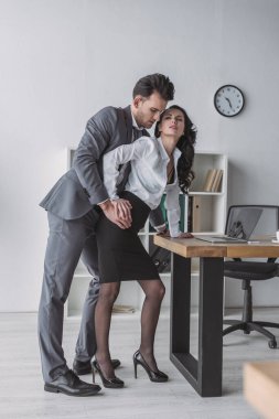 handsome businessman touching seductive secretary in office clipart