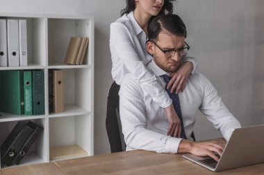 Seksi bir iş kadınının dizüstü bilgisayarla çalışırken cesareti kırılan bir meslektaşı kucaklaması.