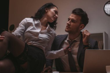 Seksi sekreterin masada oturup yakışıklı iş adamının kravatına dokunduğu seçici odaklanma.
