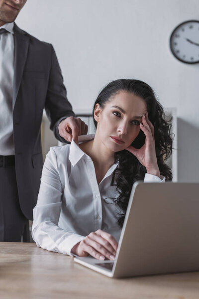 cropped view of businessman touching blouse of bored secretary sitting at workplace