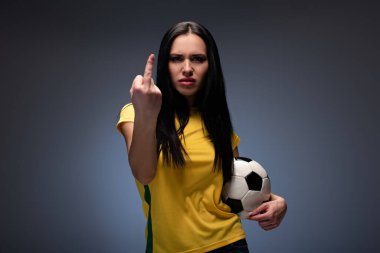 angry female football fan holding ball while showing middle finger on grey clipart