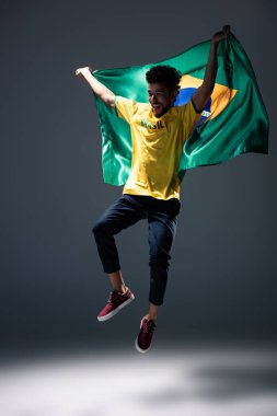 Heyecanlı Afro-Amerikan futbol fanatiği Brezilya bayrağıyla gri üzerine atlıyor