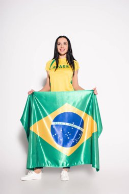Gülümseyen bayan futbol taraftarı gri üzerinde Brezilya bayrağı taşıyor