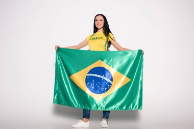 Çekici gülümseyen bayan futbol fanatiği gri üzerinde Brezilya bayrağı tutuyor
