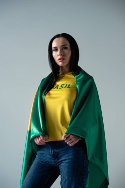 Brezilya bayraklarına sarılmış güzel bayan futbol fanatiği. Gri üzerine izole edilmiş.