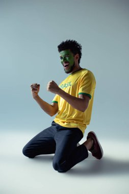 Duygusal Afro-Amerikan futbol fanatiği. Yüzü Brezilya bayrağı gibi boyanmış. Gri üzerine diz çökmüş.