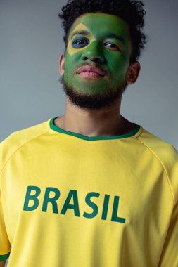 Yüzü Brezilya bayrağı gibi boyanmış, gri üzerine izole edilmiş Afro-Amerikan futbol fanatiği.
