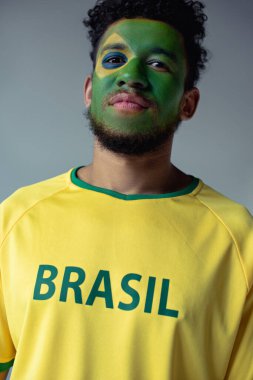 african american football fan with face painted as brazilian flag isolated on grey clipart