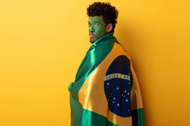 Afrikalı Amerikan futbol fanatiği, sarı bayrakla Brezilya bayrağına sarılı yüzü boyalı.