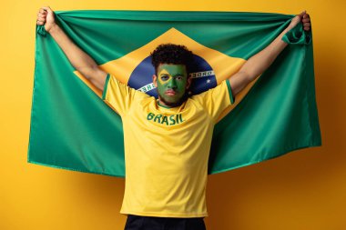african american football fan with painted face holding brazilian flag on yellow clipart