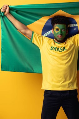 Ciddi bir Afrika Amerikan futbol fanatiği. Yüzü boyalı. Sarı bayrakla Brezilya bayrağı taşıyor.