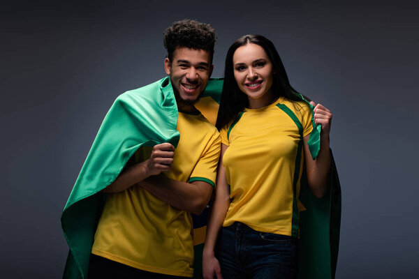 многонациональная пара счастливых футбольных болельщиков с бразильским флагом на сером
