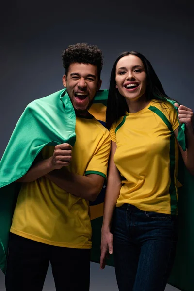 ブラジルの国旗がグレーの興奮したサッカーファンの多民族カップルが — ストック写真