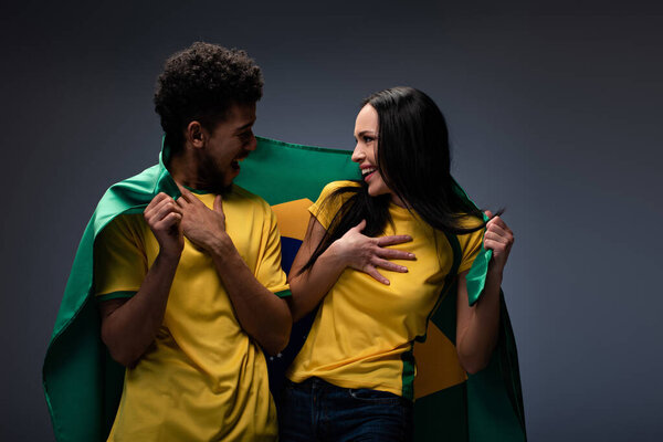 многонациональная пара счастливых футбольных болельщиков с бразильским флагом на сером
