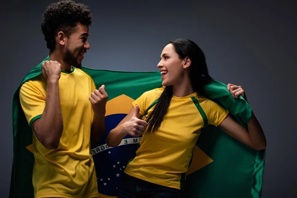 multicultural couple of excited football fans with brazil flag on grey
