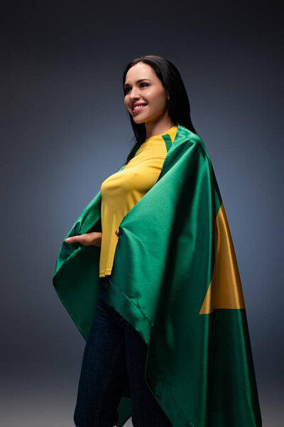 улыбающаяся футбольная фанатка, завернутая в бразильский флаг на сером
