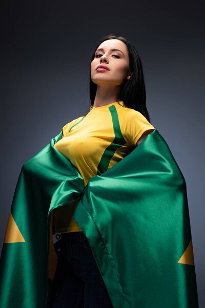 гордая футбольная фанатка, завернутая в бразильский флаг на сером
