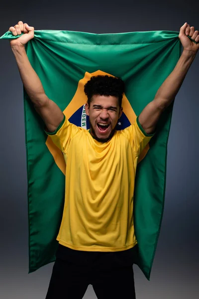 Podekscytowany Amerykański Fan Piłki Nożnej Trzyma Brazylijską Flagę Szarości — Zdjęcie stockowe