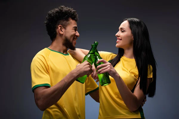 Smiling Multiethnic Couple Football Fans Yellow Shirts Clinking Bottles Beer — Stock Photo, Image