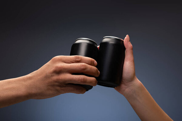 cropped view of couple clinking with black cans on gray