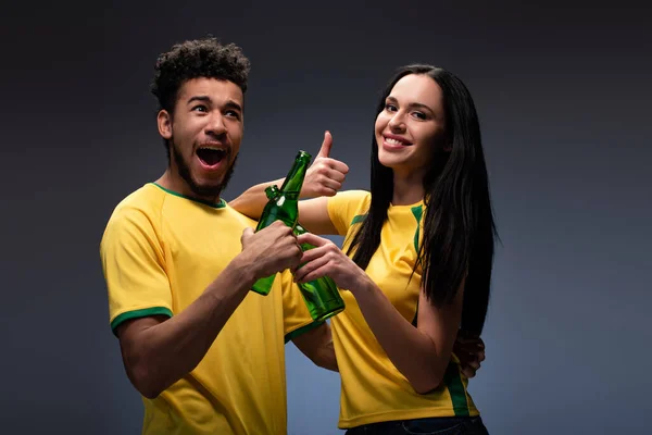 Excited Multiethnic Couple Football Fans Yellow Shirts Clinking Bottles Beer — Stock Photo, Image
