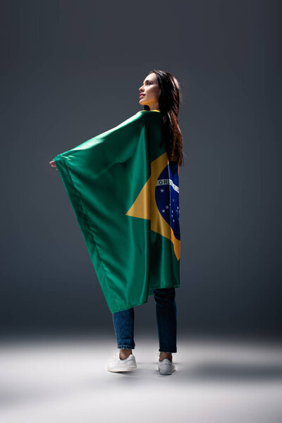 красивая футбольная фанатка, завернутая в бразильский флаг на сером
