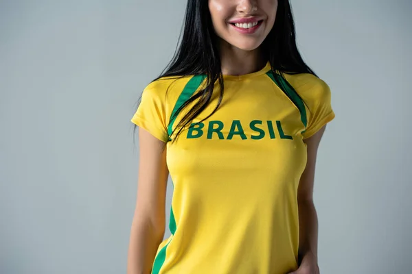 ブラジルのサインがグレーに孤立している黄色のTシャツで幸せなサッカーファンのクロップドビュー — ストック写真