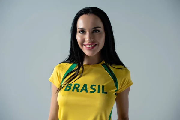 黄色のTシャツにブラジルのサインがグレーに孤立した女性サッカーファンの笑顔 — ストック写真