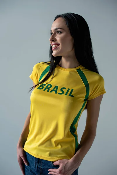 黄色のTシャツにブラジルのサインがグレーに孤立した女性サッカーファンの笑顔 — ストック写真