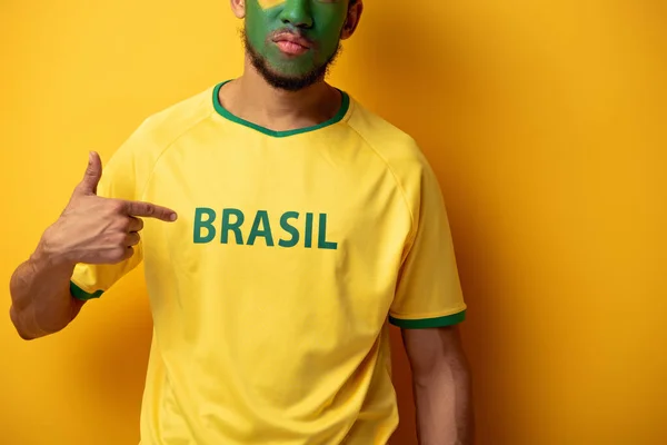 黄色のブラジルの看板のTシャツを指している顔を描いたサッカーファンのクロップドビュー — ストック写真