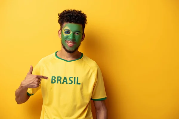 Улыбающийся Африканский Футбольный Фанат Раскрашенным Лицом Указывающим Футболку Бразильским Знаком — стоковое фото