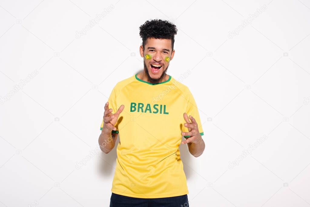 emotional african american football fan in yellow t-shirt with brazil sign gesturing and shouting on grey