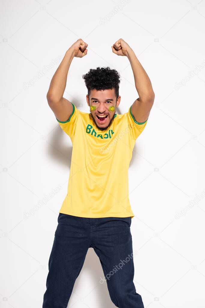 african american football fan in yellow t-shirt with brazil sign shouting and gesturing on grey