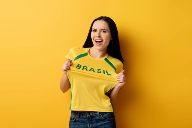 excited female football fan in yellow t-shirt with brazil sign on yellow   clipart